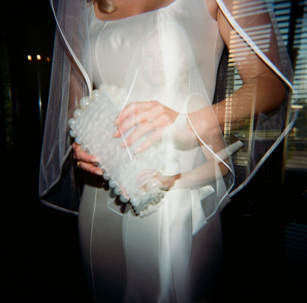 Detail of bride holding white floral bouquet with Pearl veil and satin dress back bow detail.