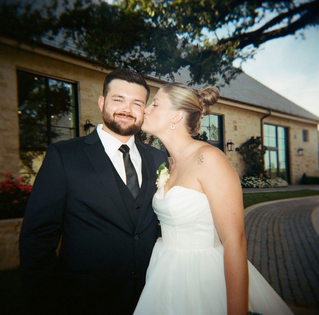 Close-up portrait of bride in strapless wedding dress with delicate shoulder tattoo next to groom in black suit and tie at The Bower in Edmond, Oklahoma.