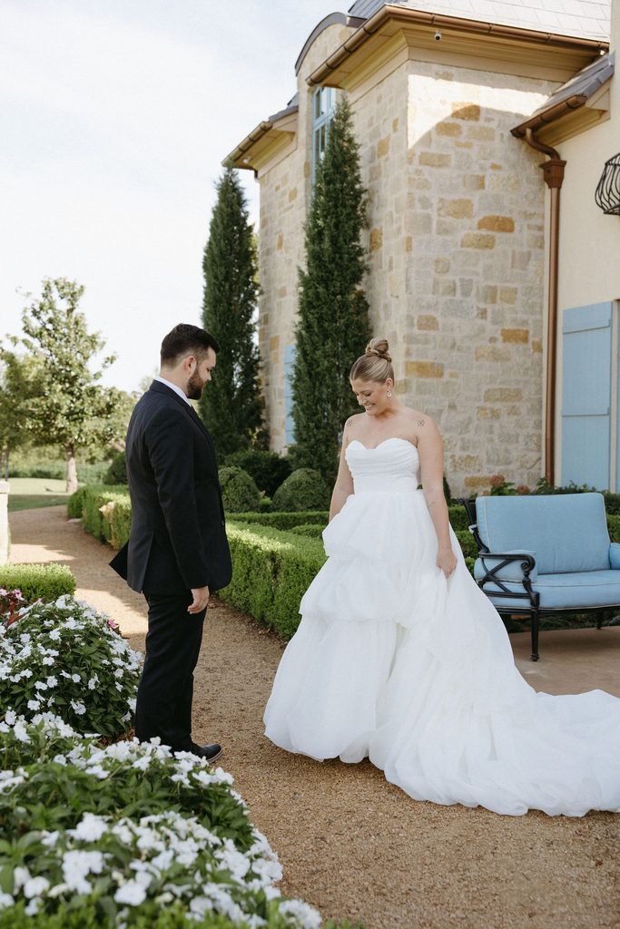 Alt text: Bride in strapless layered tulle wedding dress and groom in black suit sharing a first look outdoors at The Bower in Edmond, Oklahoma.