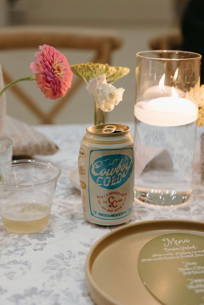 Wedding reception table detail with pink zinnias in a bud vase, votive candle, and beer can at The Bower in Edmond, Oklahoma.