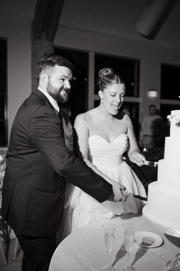 Black and white candid reaction shot of bride and groom sitting at their wedding reception dinner.