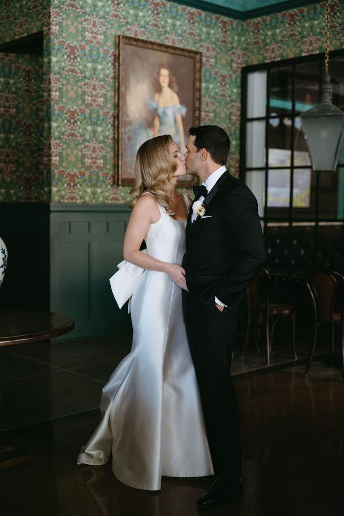 Bride and groom kissing inside bridal suite with green patterned wallpaper at historic Oklahoma Hall of Fame venue.