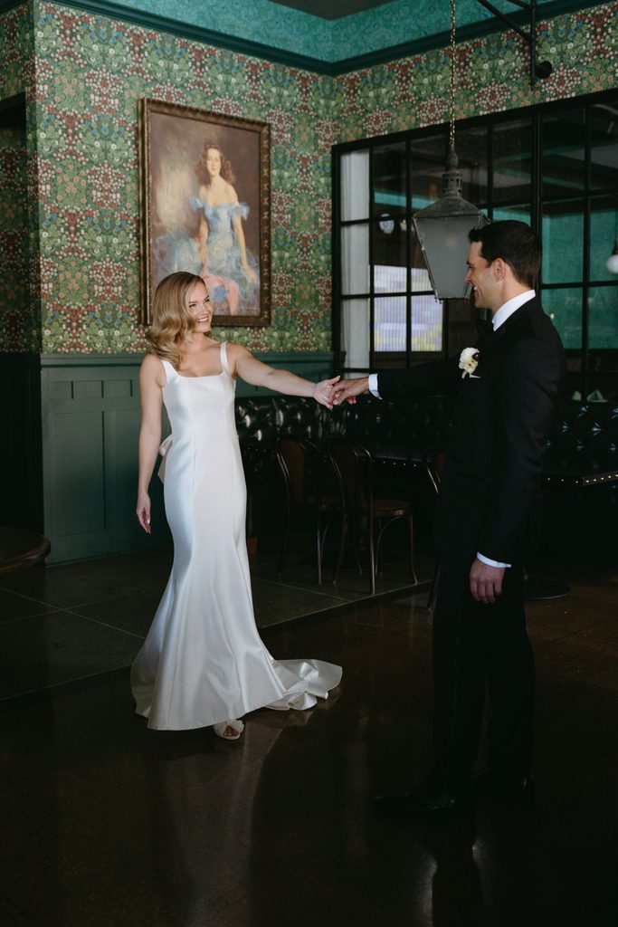 Bride smiling in green patterned wallpaper bridal suite holding hands with groom at historic Oklahoma Hall of Fame.