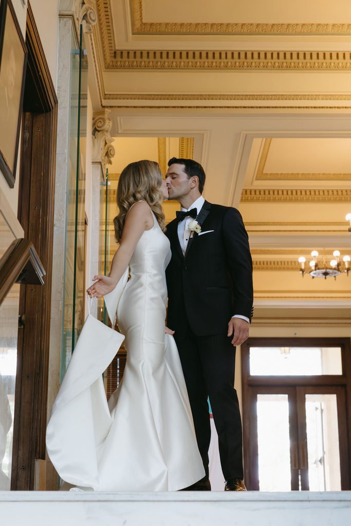 Bride and groom kissing inside marble hallway with columns at historic Oklahoma Hall of Fame venue.