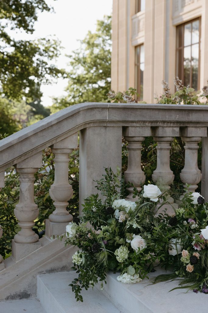Outdoor reception setup with floral arrangements on stone staircase railing at Gaylord-Pickens Museum in Oklahoma City.