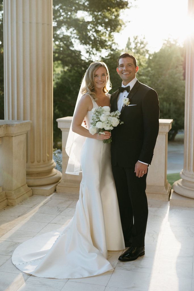 Bride and groom posing together in front of stone columns in golden hour light at historic Oklahoma Hall of Fame venue.