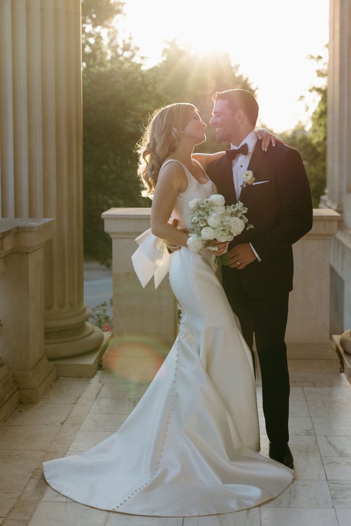 Bride and groom leaning in for a kiss framed by golden sunlight between stone columns at Oklahoma Hall of Fame.