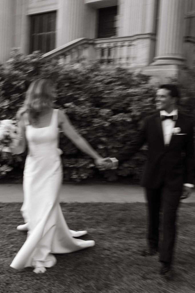 Black and white candid photo of bride and groom walking hand-in-hand outside Gaylord-Pickens Museum venue in Oklahoma City.