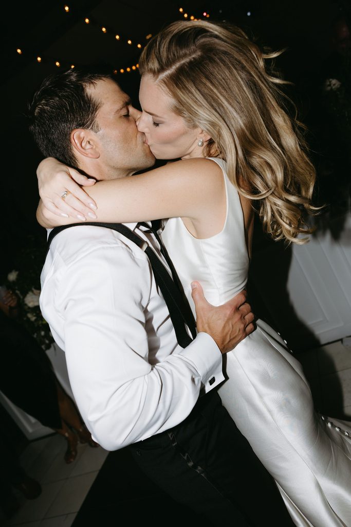 Groom holding bride in a dip kiss under string lights during outdoor evening wedding reception at Gaylord-Pickens Museum in Oklahoma City.