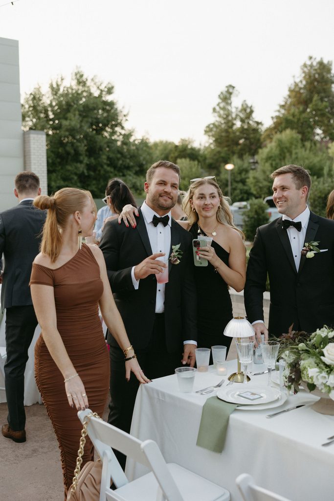 Wedding guests mingling during outdoor evening reception near black-and-white checkered dance floor and string lights at Gaylord-Pickens Museum in Oklahoma City.