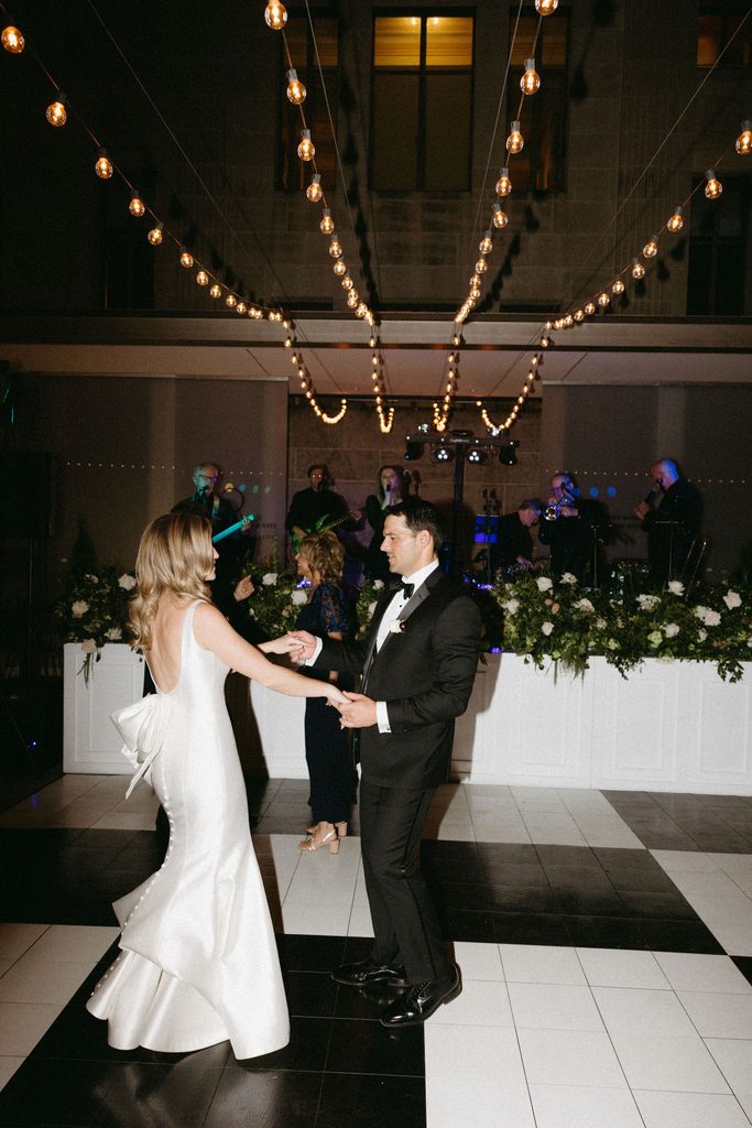 Bride and groom dancing hand-in-hand on black-and-white checkered dance floor during evening reception at Oklahoma Hall of Fame.