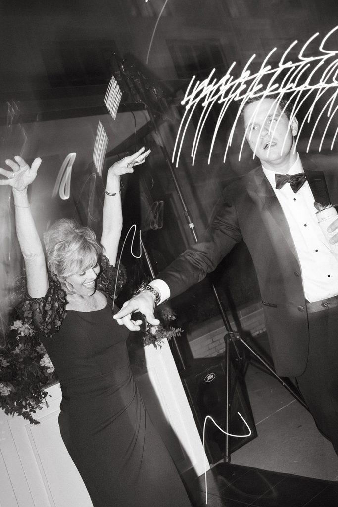 Black and white photo of wedding guests dancing with hands in the air during outdoor reception at Oklahoma Hall of Fame.