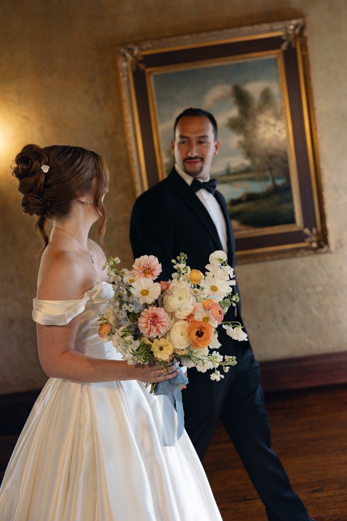 Bride and groom posing together inside an elegant room at Dresser Mansion, framed by classic gold portrait frames and dark wood architectural detailing.