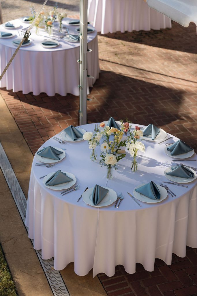 Round outdoor reception table at Dresser Mansion set with white linens, sage green napkins, floral centerpieces, and place settings.