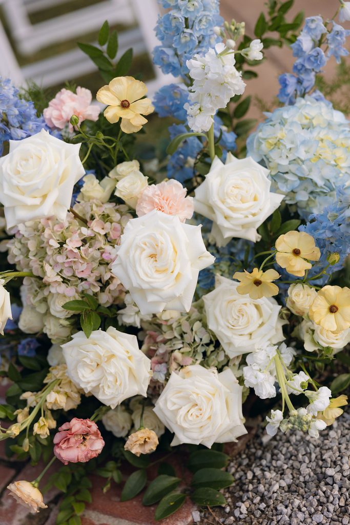 Close-up of a wedding floral arrangement featuring pastel yellow, blush, white, and soft blue flowers arranged outside at Dresser Mansion in Tulsa.