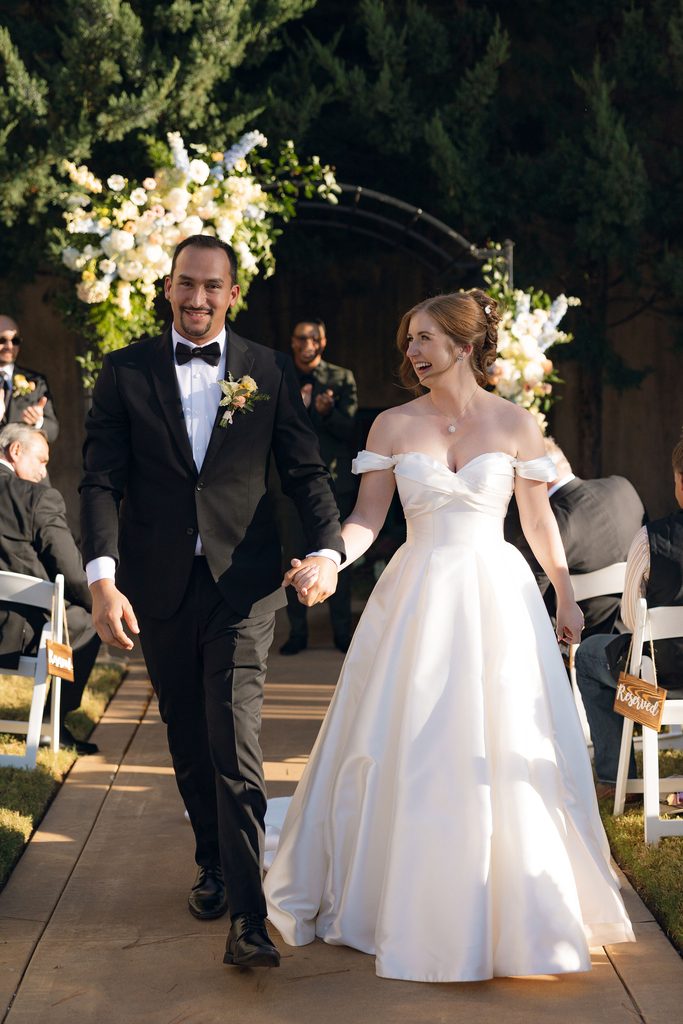 Bride and groom smiling and walking down the aisle together after their outdoor wedding ceremony at Dresser Mansion in Tulsa.