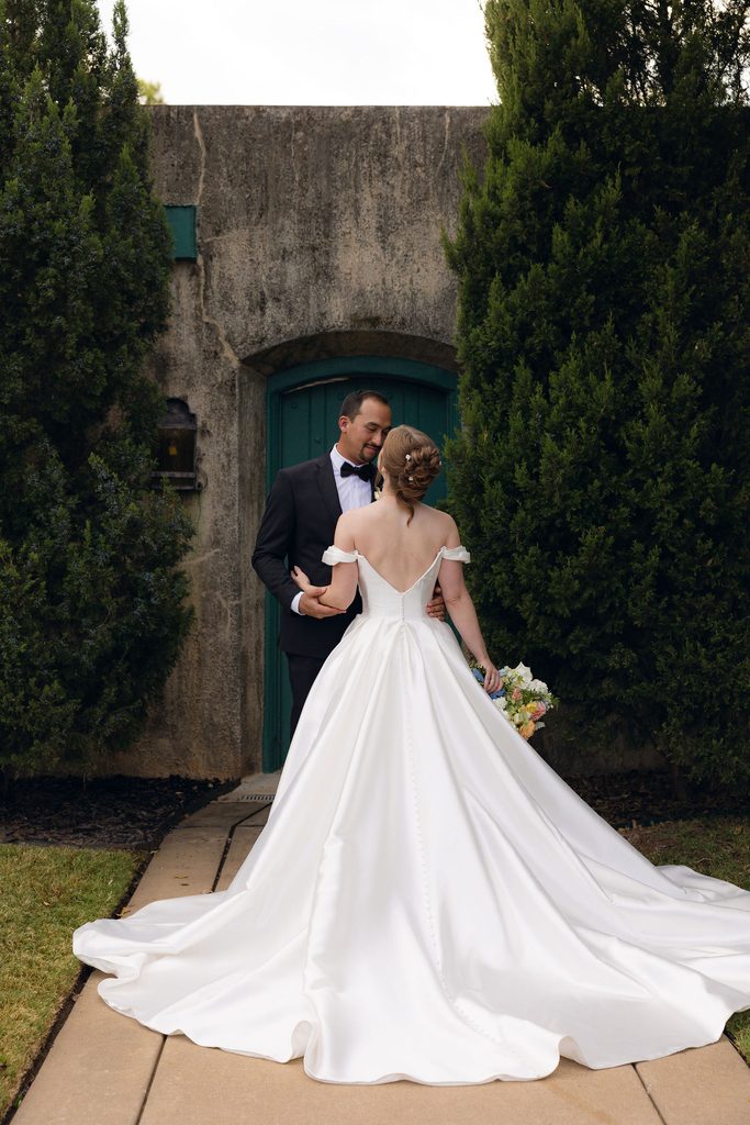 Bride and groom posing together on a stone pathway outside the stone exterior and arched green doorway of Dresser Mansion in Tulsa.