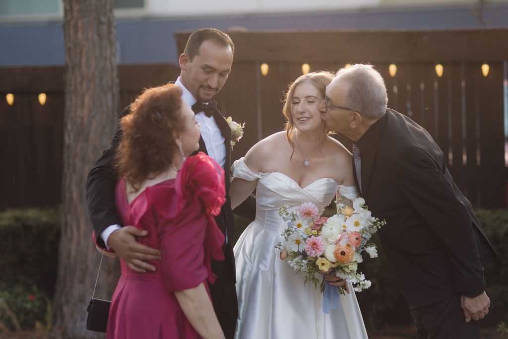 Bride in an off-the-shoulder gown smiling warmly while interacting with family and guests during a wedding reception at Dresser Mansion.