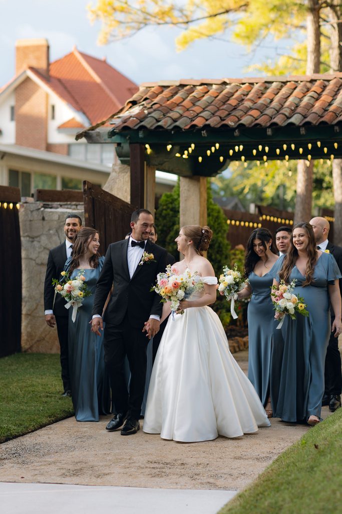 Bride and groom standing outdoors with their wedding party under string lights on the grounds of Dresser Mansion in Tulsa.